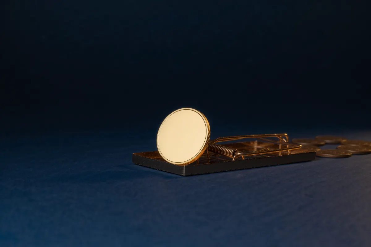 Blank gold coin placed next to a mouse trap on a dark navy surface